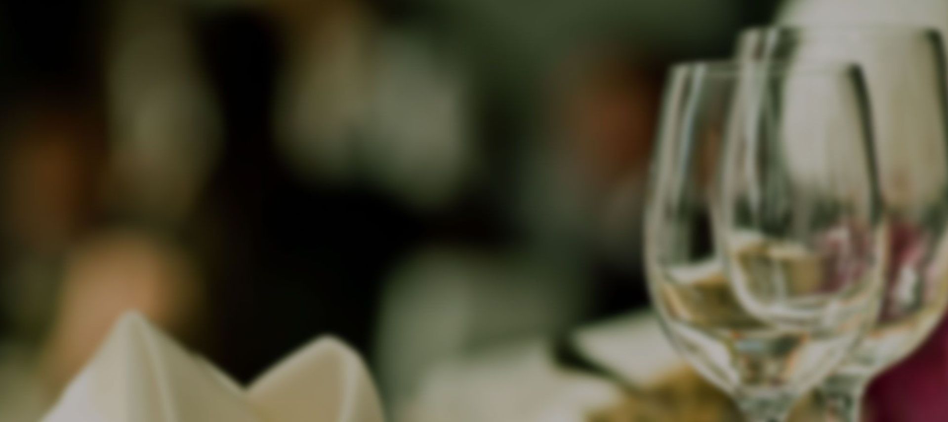 Blurred close-up of a set table with wine glasses and napkins.